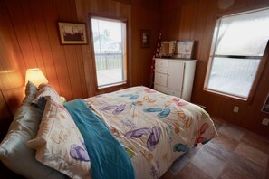 A bedroom with a bed, two windows, a dresser, and a lamp.