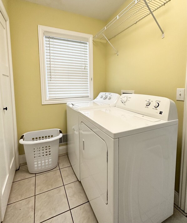 A laundry room with a front-loading washer and dryer, a laundry basket, a window with blinds, and a metal drying rack. - Beautiful Lakefront Home- Crooked Lk-Petoskey/Harbor Springs/Nubs- boat/bike/ski (Conway)