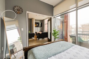Une chambre moderne avec un grand lit, un miroir, une horloge et une vue sur un espace de vie comprenant un canapé et un téléviseur.