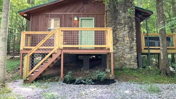 A wooden cabin with a stone chimney, a wooden deck with a railing, and a green door. - Creekside Couple's Retreat at Cool Waters (Cosby)