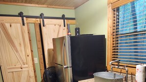 A kitchen with a wooden floor, a black refrigerator, a sink, and a window with blinds. - Creekside Couple's Retreat at Cool Waters (Cosby)