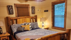 A wooden-framed bed with patterned bedding, a nightstand with a lamp, a ceiling fan, and a window with blinds. - Creekside Couple's Retreat at Cool Waters (Cosby)