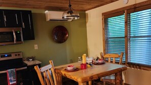 A wooden dining table with chairs, a hanging light fixture, a microwave, and a stove in a kitchen with wooden flooring. - Creekside Couple's Retreat at Cool Waters (Cosby)