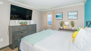 Un dormitorio con cama, cómoda, televisor y ventana con cortinas.