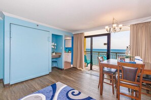 Ein Zimmer mit Essbereich, einer Küche und einer Glastür, die auf einen Balkon mit Meerblick führt.