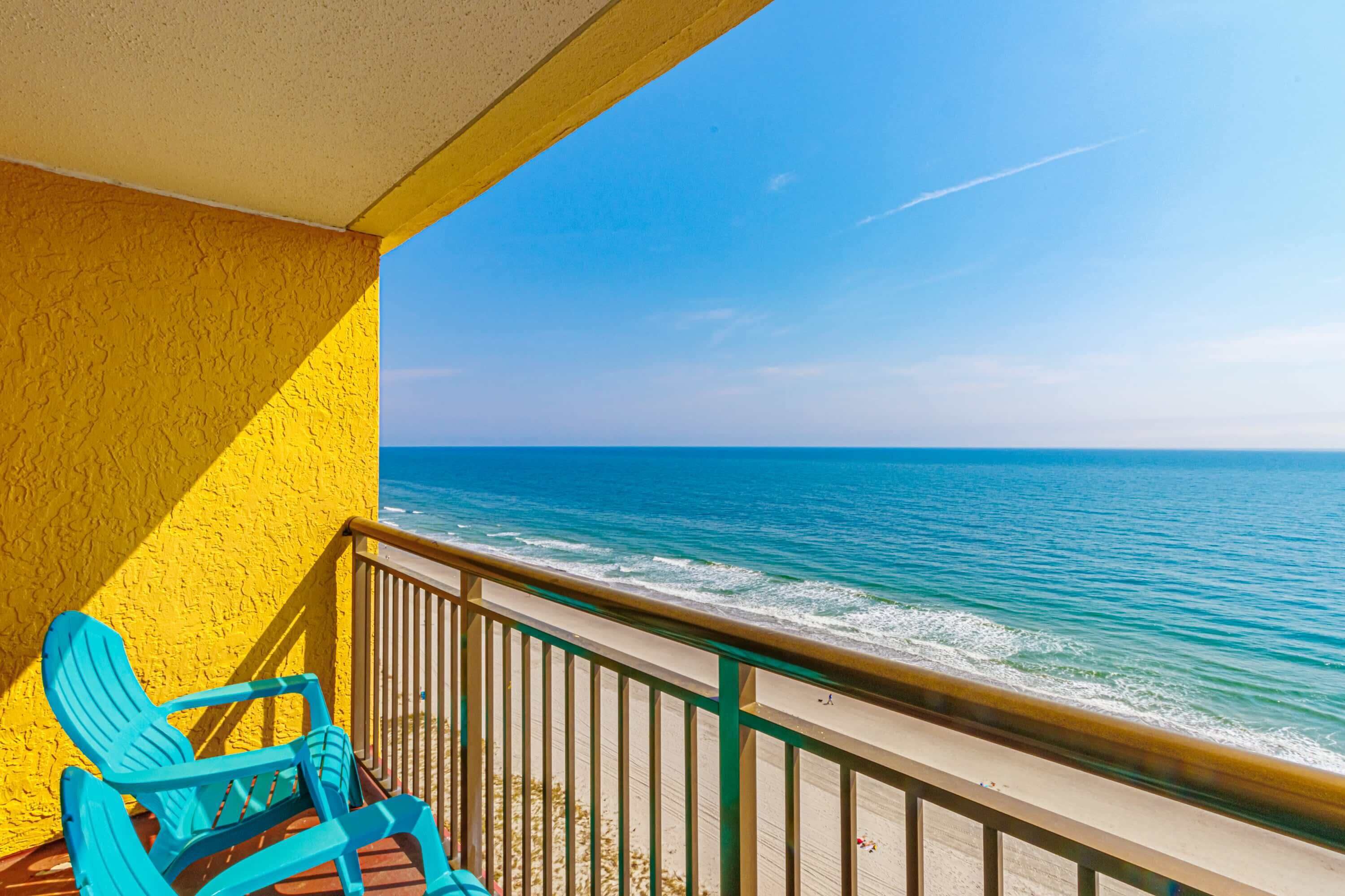 Un balcon avec vue sur l’océan, une chaise bleue et un mur jaune.