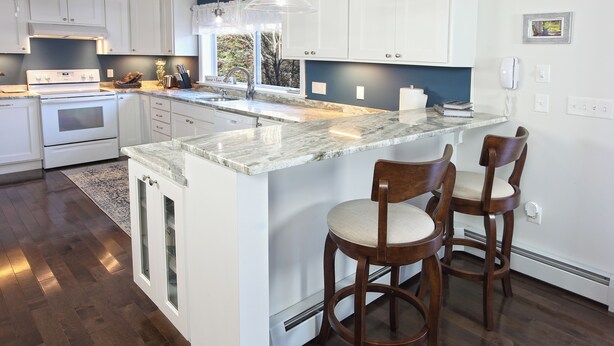 A kitchen with a large island, white cabinets, and a dark wooden floor.