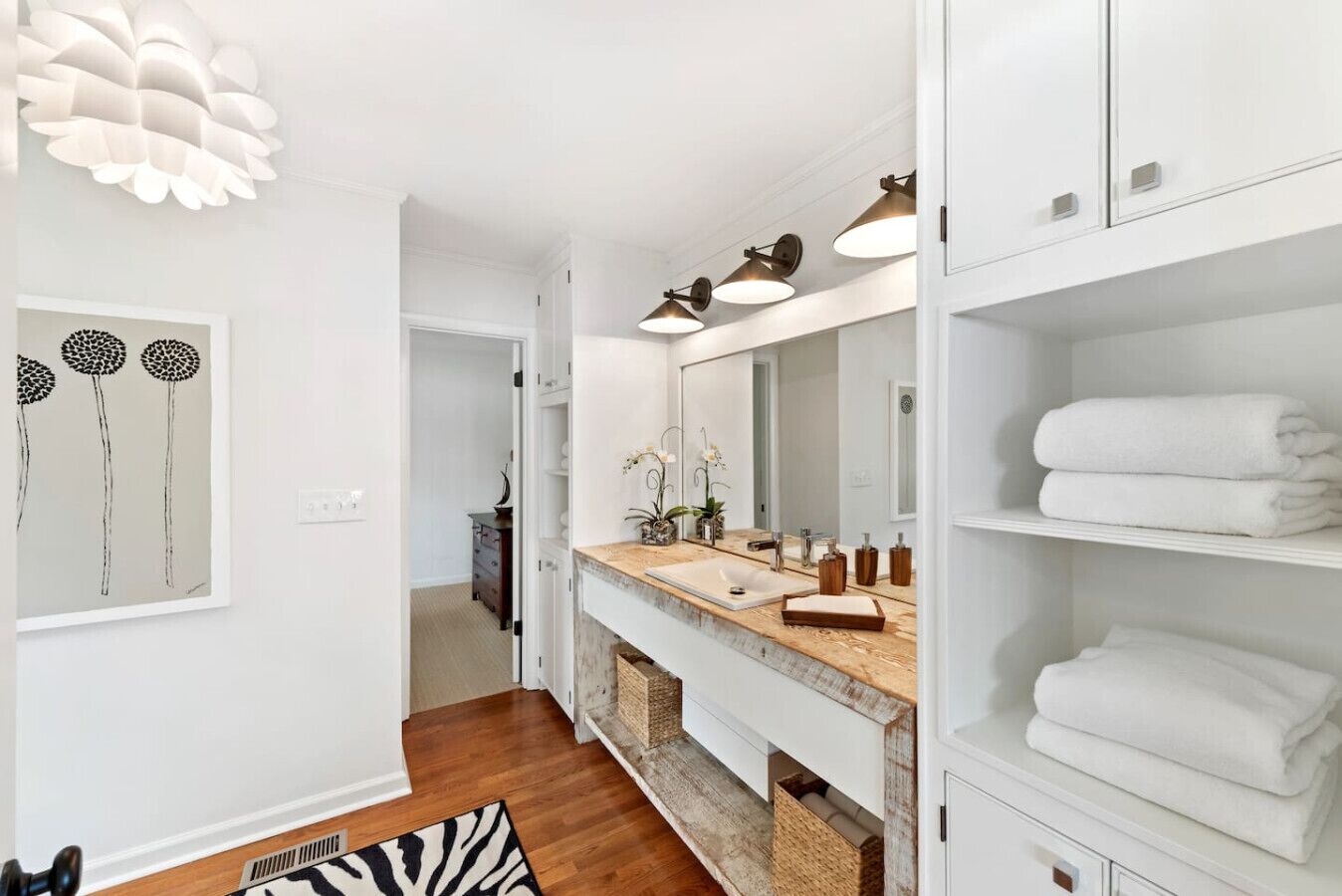 A modern bathroom with a wooden vanity, white cabinetry, and a large mirror.