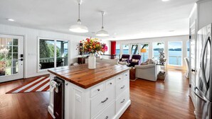 Une cuisine moderne avec un îlot central en bois, des meubles blancs et une vue sur l’extérieur.