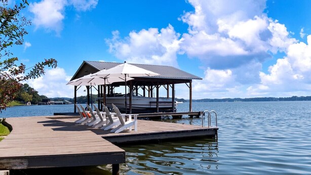 Une jetée en bois avec des chaises longues et un pavillon abrité, le tout au bord d’un lac paisible.