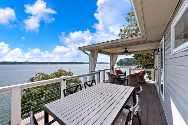 A covered deck with a table and chairs, overlooking a lake.