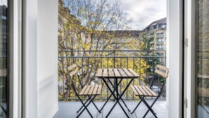 A balcony with a wooden table and chairs, surrounded by a metal railing, overlooking a residential area with trees and buildings. - Airy Vorstädte 3.5 Room w/ W/D & Storage, 2 min to Market, by Blueground (Basel)