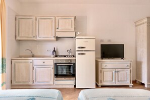 A compact kitchen with a refrigerator, stove, oven, and a television on a cabinet.