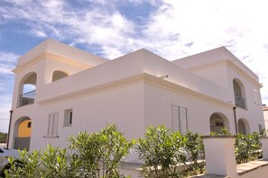 A white building with arched windows and balconies, surrounded by greenery.