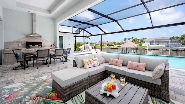 Un espacio exterior con piscina, una barbacoa y un área de descanso con cojines.