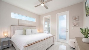 Un dormitorio con cama, ventilador de techo, mesita de noche, planta en maceta y vistas al exterior.