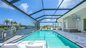 Una piscina con techo de cristal, sillas de descanso y vistas a un canal y casas.