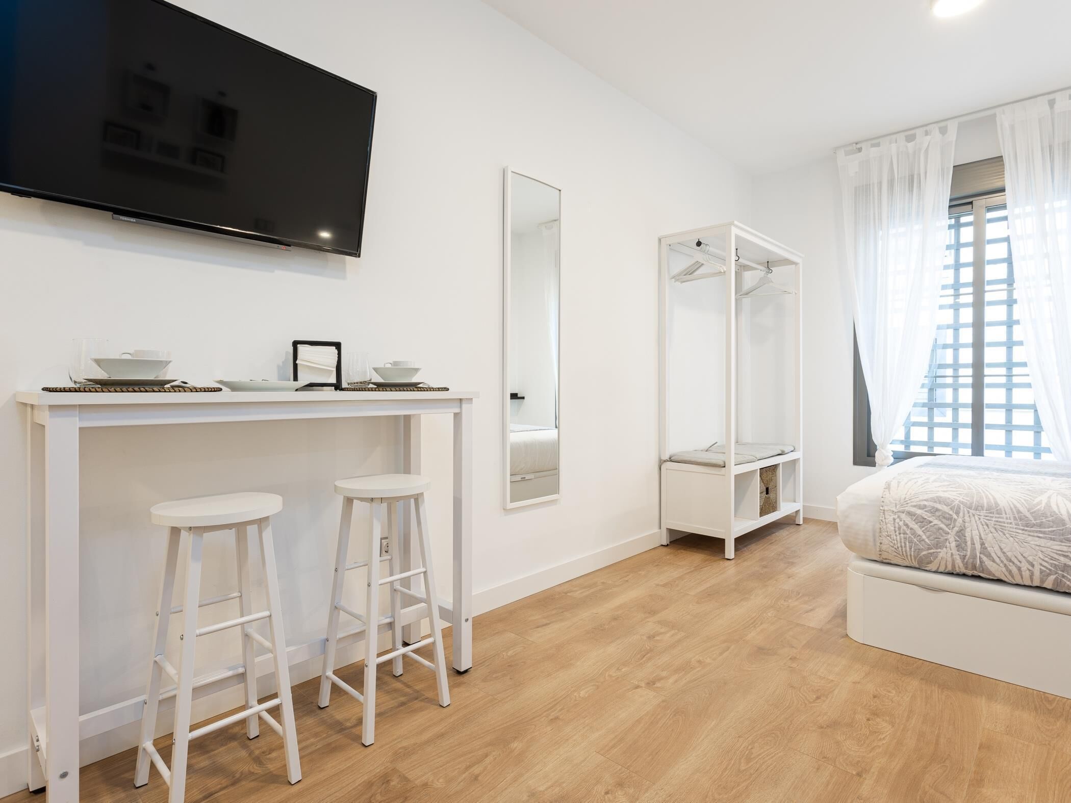 Une chambre moderne comprenant un lit, un téléviseur, une armoire et un bureau avec des tabourets.