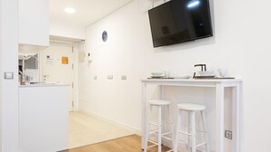 Una cocina moderna con televisor de pantalla plana, taburetes de bar blancos y una pequeña mesa de comedor.