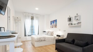 Un dormitorio moderno y minimalista con una cama, mesitas de noche, un sofá negro y una zona de comedor con mesa y sillas.