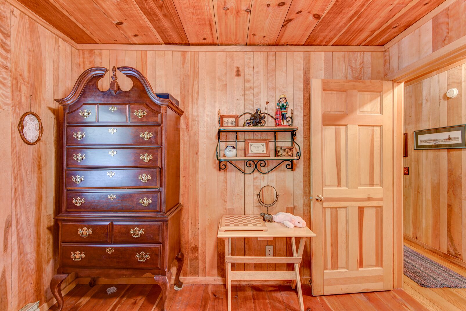 A wooden-paneled room with a large wooden dresser, a small table with a mirror, and a door.