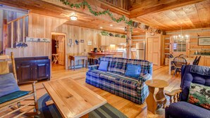 Ein gemütliches Blockhauss-Interieur mit Holzboden, einem karierten Sofa, einem Esstisch und einer Küchenzeile.