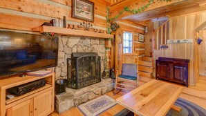Ein gemütliches Blockhaus-Interieur mit Kamin aus Stein, Holzwänden, einem Fernseher und einem Essbereich.