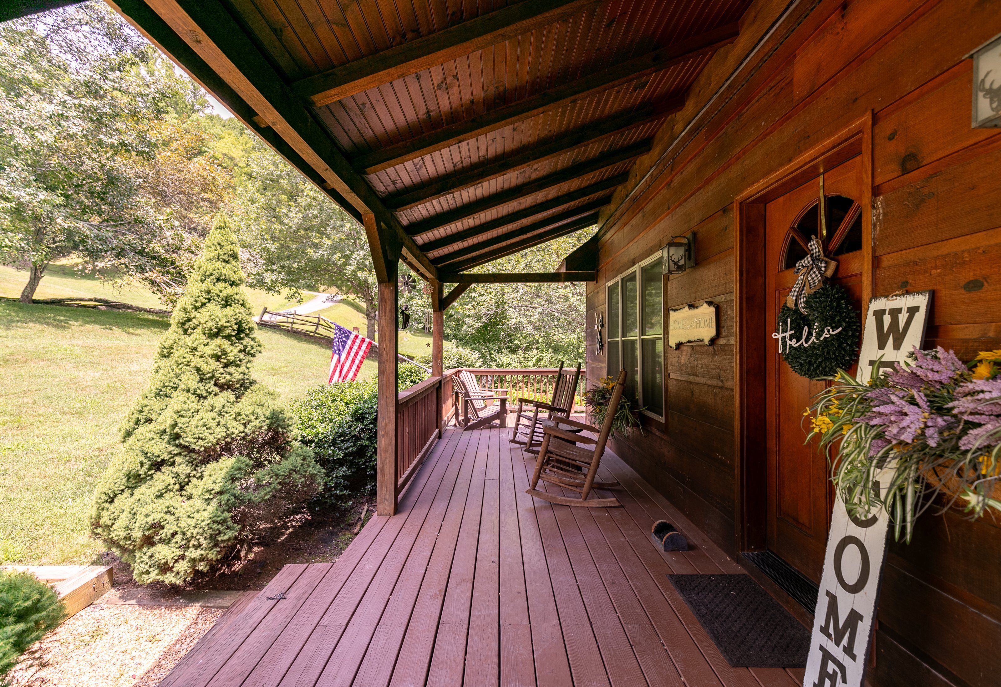 A wooden porch with rocking chairs, a welcome sign, and an American flag.