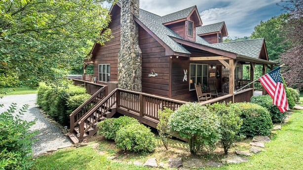 A wooden cabin with a stone chimney, a porch, and an American flag. - Country Life - hot tub, wood burning fireplace, pet friendly (Vilas)
