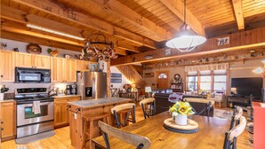 A spacious kitchen with wooden cabinets, a stainless steel stove, and a dining area with a wooden table and chairs. - Country Life - hot tub, wood burning fireplace, pet friendly (Vilas)