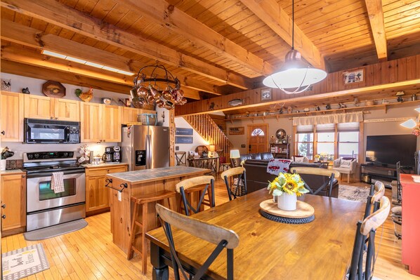 A spacious kitchen with wooden cabinets, a stainless steel stove, and a dining area with a wooden table and chairs. - Country Life - hot tub, wood burning fireplace, pet friendly (Vilas)