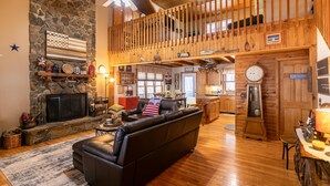 A spacious living area with a stone fireplace, a black leather sofa, and a wooden ceiling. - Country Life - hot tub, wood burning fireplace, pet friendly (Vilas)