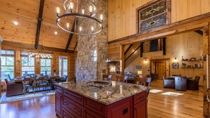 A spacious kitchen with a large island, wooden floors, and a stone accent wall. - Papa's View - Pet Friendly Luxury Log Cabin in Valle Crucis with Views and Hot Tub! (Banner Elk)
