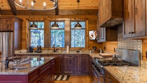 A modern kitchen with granite countertops, wooden cabinets, a stainless steel refrigerator, and a gas stove. - Papa's View - Pet Friendly Luxury Log Cabin in Valle Crucis with Views and Hot Tub! (Banner Elk)