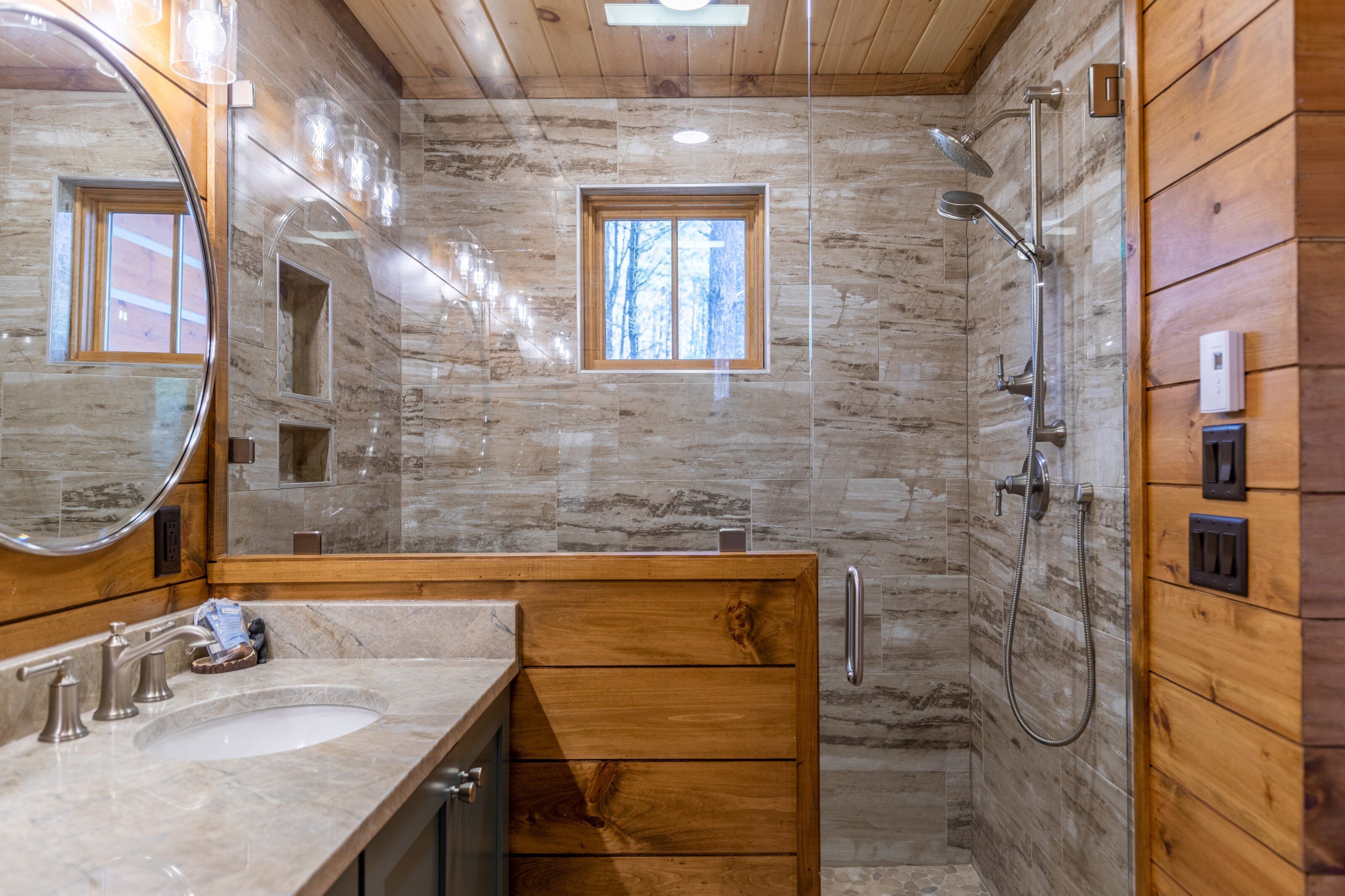 A bathroom with a wooden vanity, a sink, a mirror, a shower, and a window.