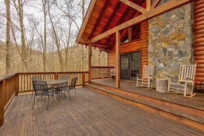 Eine Holzterrasse mit Tisch und Stühlen, eine Steinmauer und ein Blockhaus.