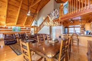 Ein geräumiges Wohnzimmer mit einem großen Holzesstisch, Ledersofas und einer Treppe, die zu einer oberen Ebene führt.