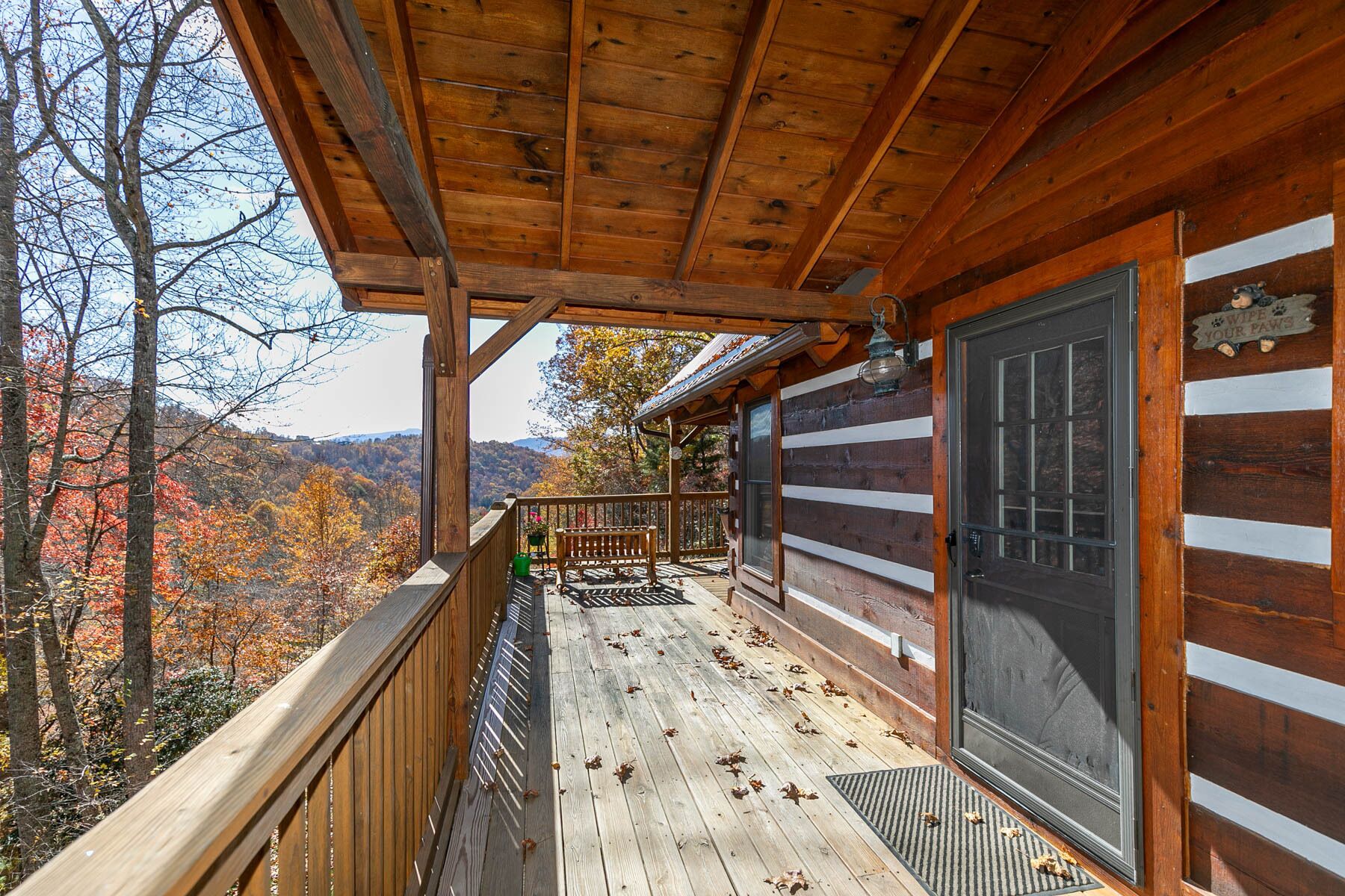 Eine Holzhütte mit Veranda, einer Tür mit Sucher und Blick auf Herbstbäume.