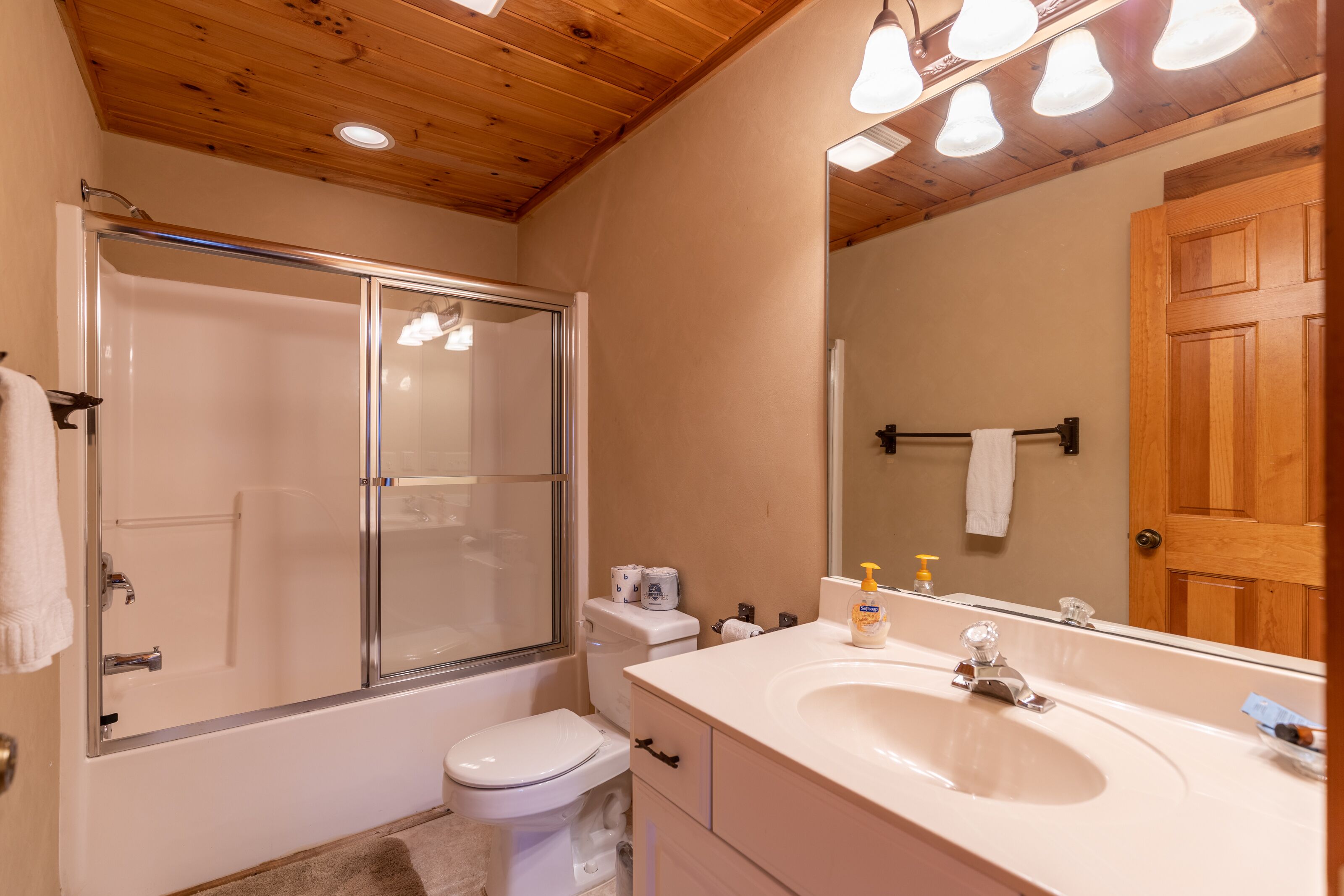 A bathroom with a glass-enclosed shower, a white toilet, a sink with a mirror, and wooden ceiling beams.
