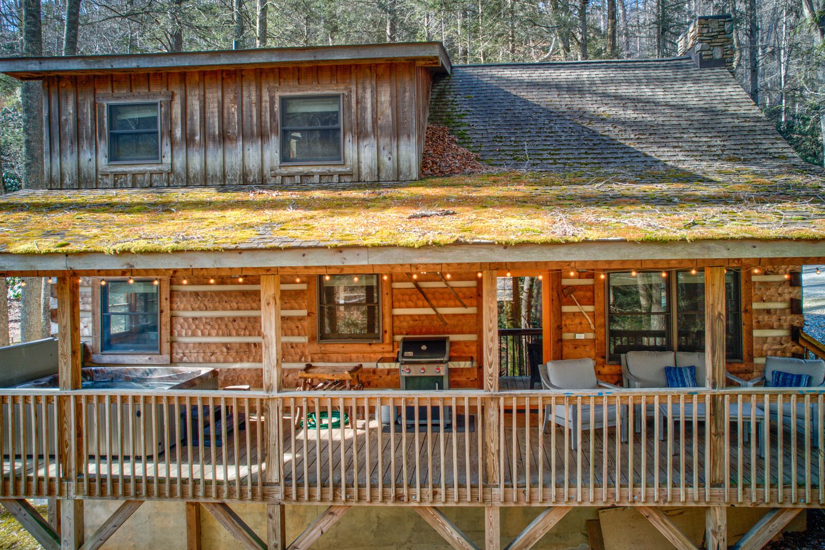 A rustic cabin with a covered porch, a stone chimney, and a deck area with outdoor seating.