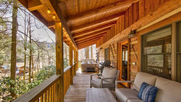 Un terrazzo in legno con divano e poltrone, un barbecue e vista sugli alberi.