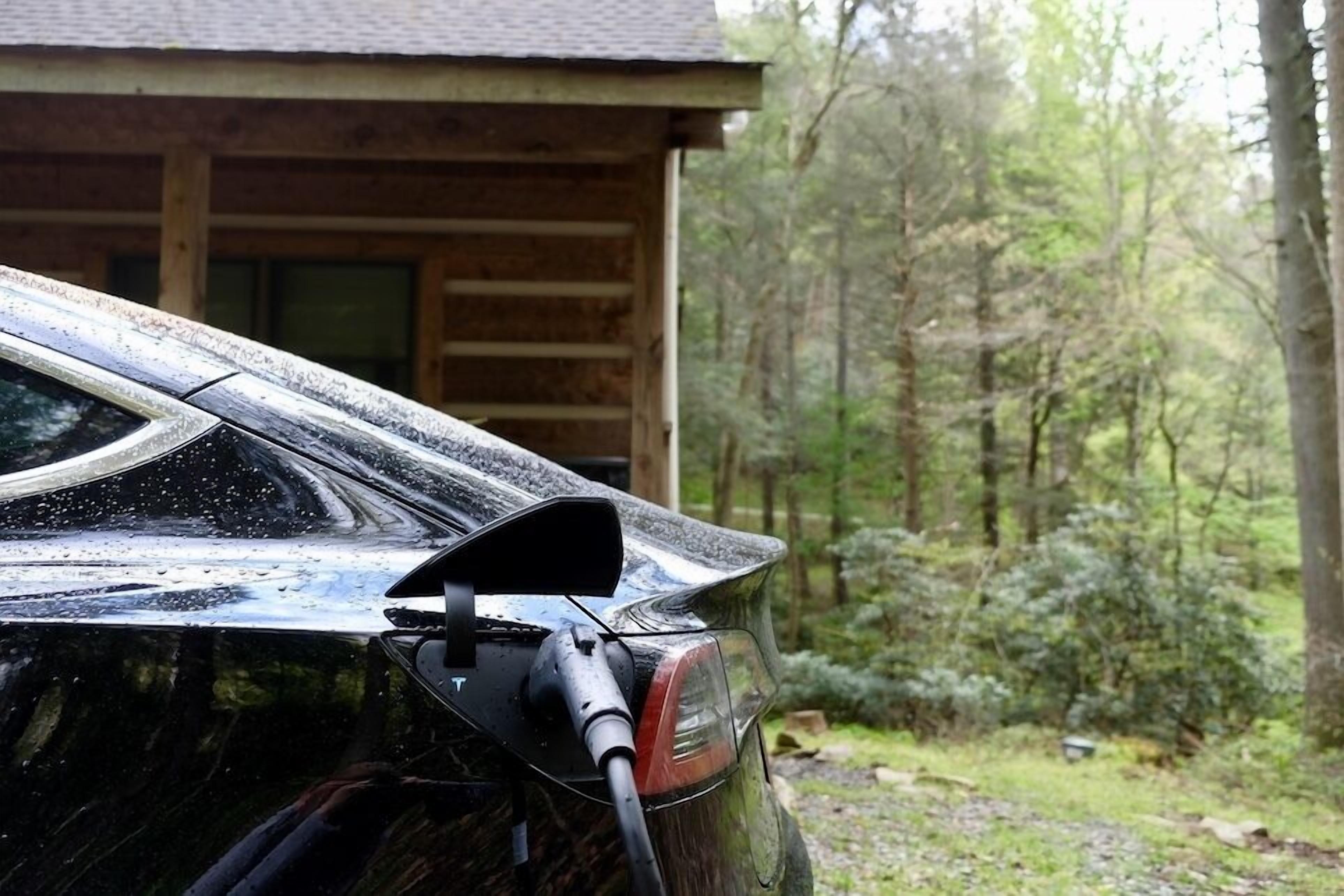 Ein schwarzes Auto vor einem Holzhaus, im Hintergrund ein Wald.
