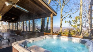 Un jacuzzi en una terraza de madera con vistas a árboles y montañas.