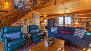 Een gezellig interieur van een blokhut met een houten trap, leren fauteuils, een blauwe bank en een eethoek.