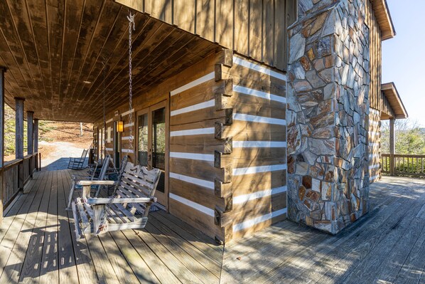 A wooden deck with a stone wall and a covered seating area. - Windsong - long range views, pet friendly, fireplace (Vilas)