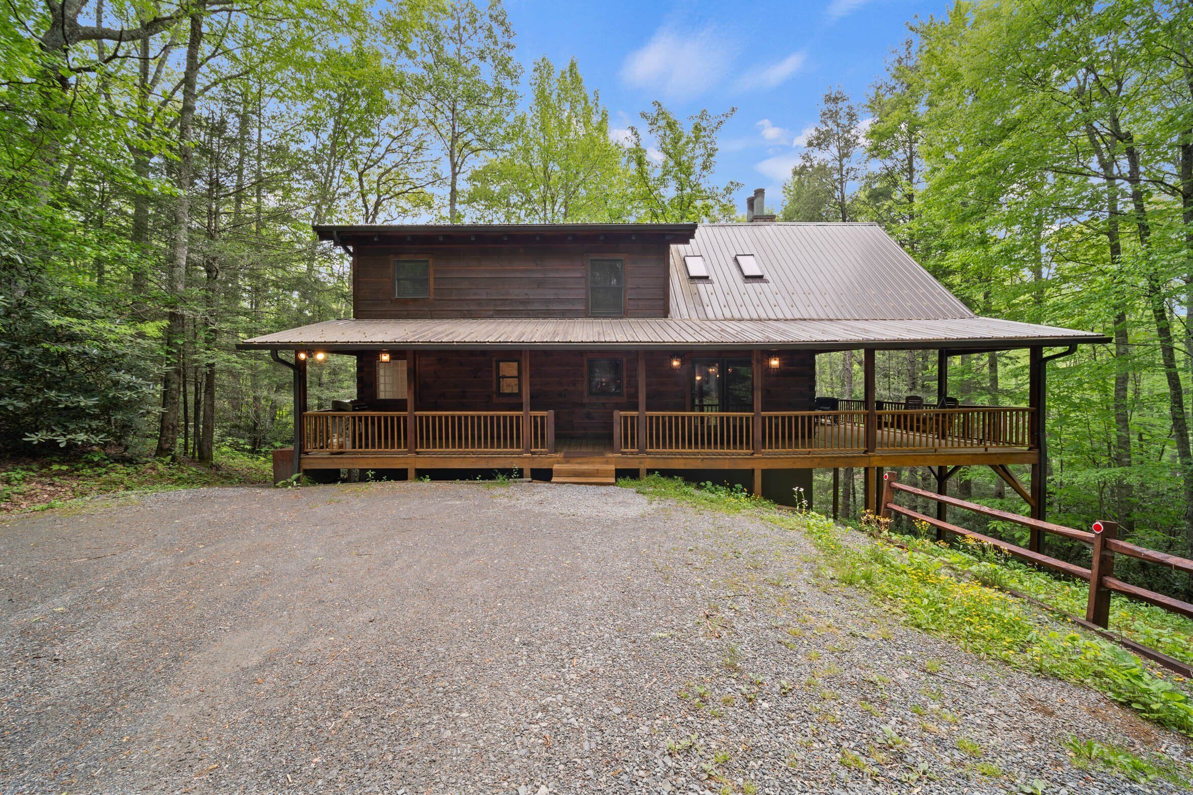 A wooden cabin with a porch, surrounded by a forest.