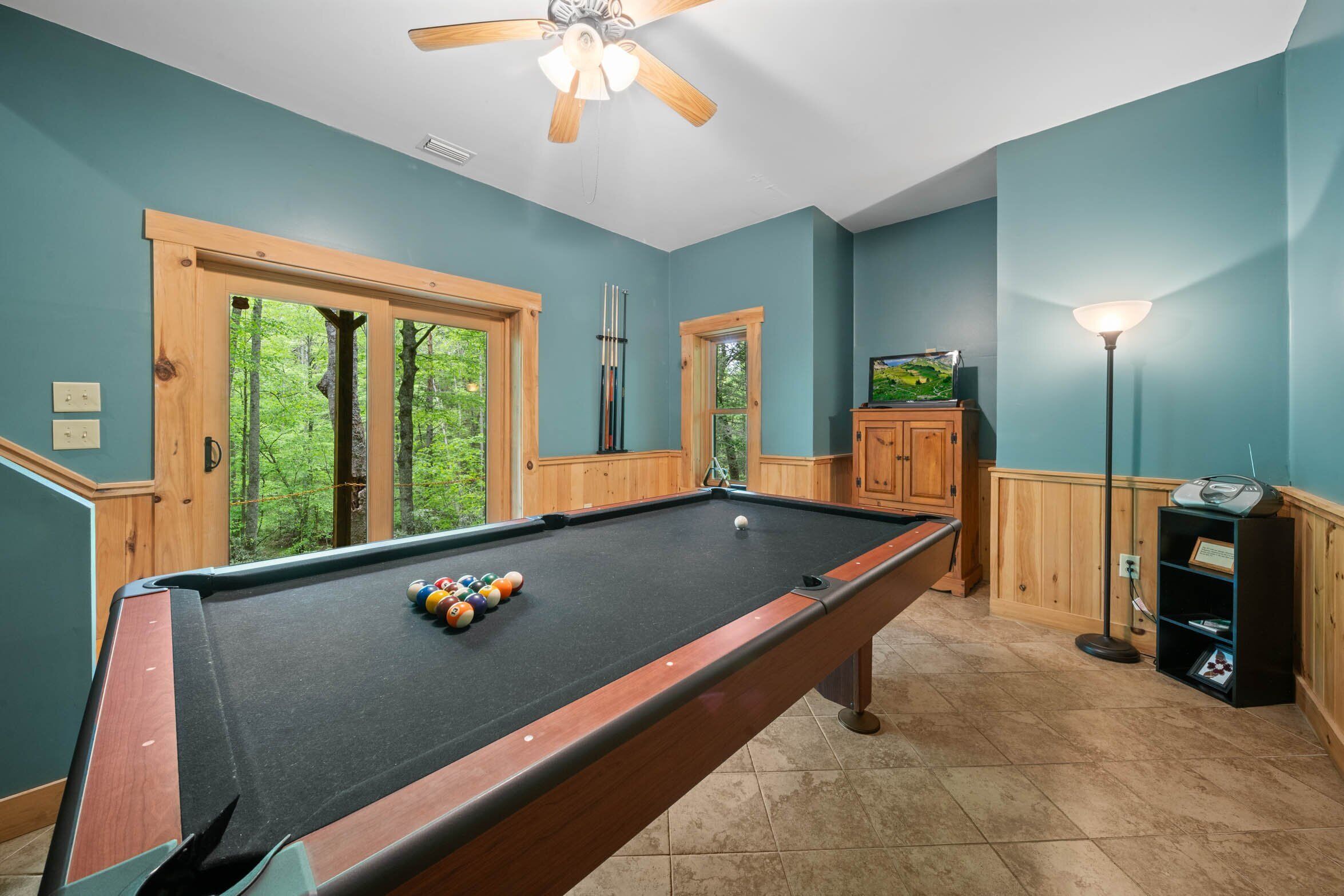 A pool table with balls, wooden cabinets, a fish tank, and a lamp in a room with teal walls and wooden trim.