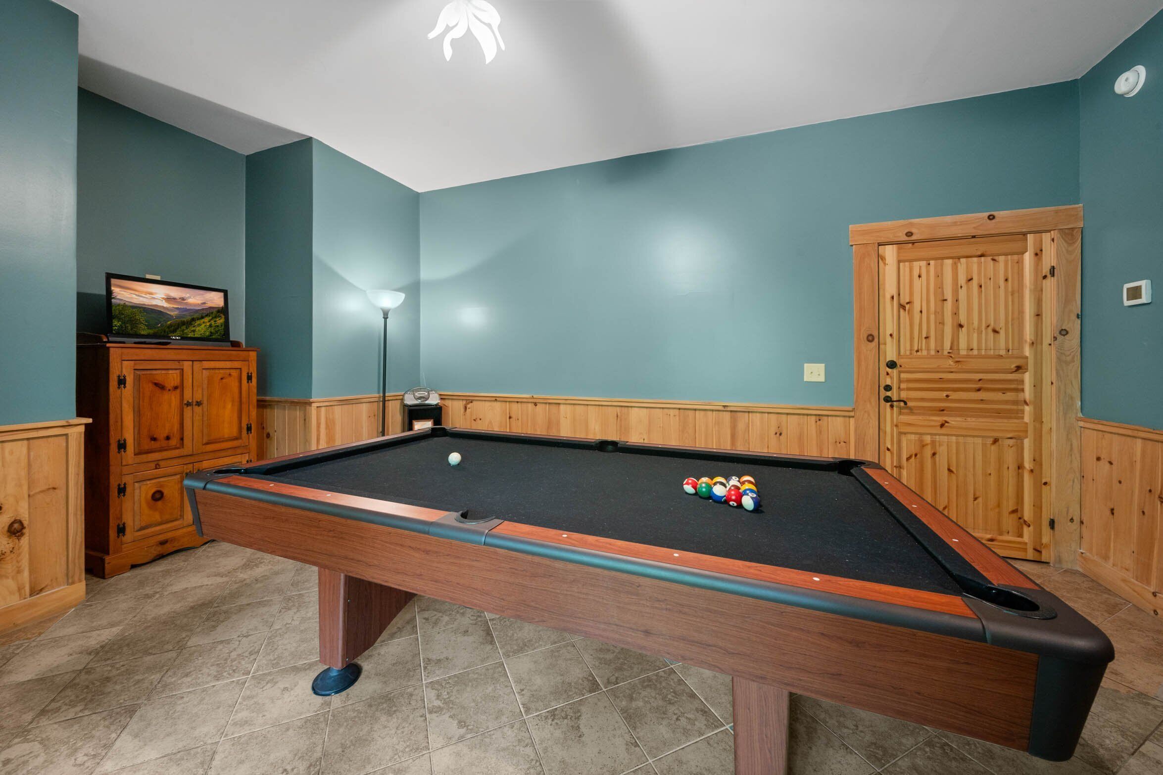 A pool table with balls, a television on a cabinet, and a lamp.
