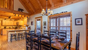 A spacious dining area with a wooden table set for six, surrounded by wooden chairs. A chandelier hangs from the ceiling, and there is a large window with blinds to the right. - Bear Creek - Beautiful home with gas fireplace, custom wood burning firepit, shuffleboard, and more! (Sugar Grove)
