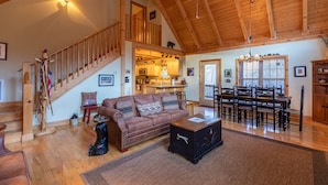 A spacious living area with a wooden staircase, a dining table with chairs, a sofa, and a coffee table. - Bear Creek - Beautiful home with gas fireplace, custom wood burning firepit, shuffleboard, and more! (Sugar Grove)